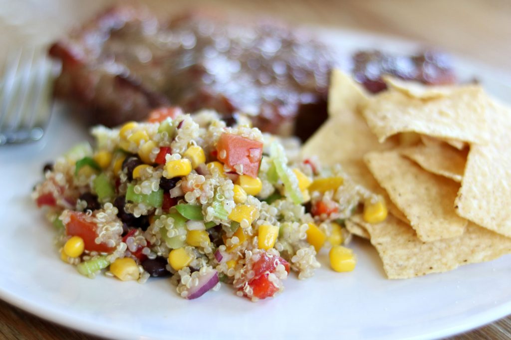 quinoa salad with avocado and tomatoes on a white plate with tortilla chips and steak
