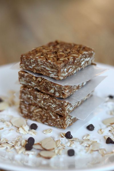 chewy oatmeal peanut butter granola bars stacked on a plate with chocolate chips almonds oats and coconut sprinkled around