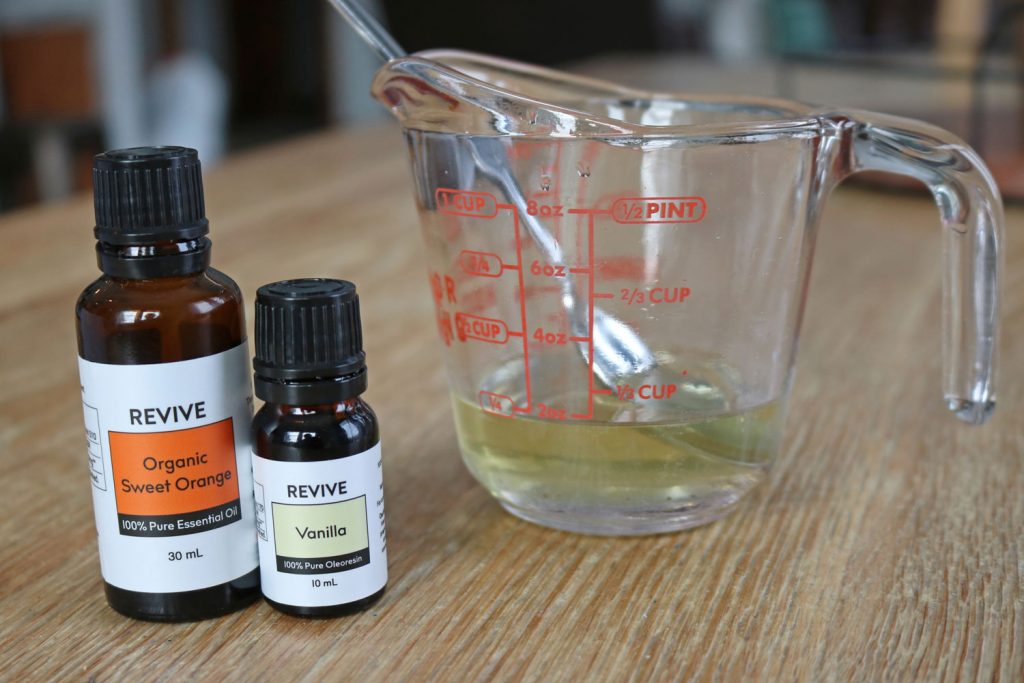 measuring cup with melted oils and bottles of essential oil for tallow lip balm